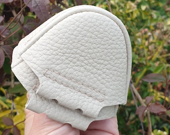 May include: A beige leather coin purse with a stitched seam and a flap closure. The purse is folded in half and held in a hand.