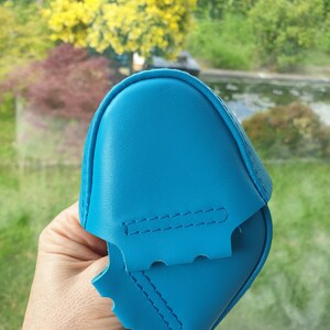 Könnte beinhalten: Zwei Stücke blaues Leder, zusammengenäht, mit einer welligen Kante. Das Leder ist weich und geschmeidig.