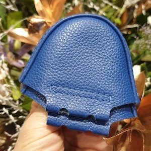 May include: A blue leather shoe horn with a curved shape and a textured surface. The shoe horn has a stitched seam around the edge.