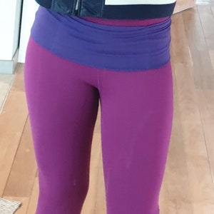 May include: Purple leggings with a blue waistband. The leggings are made of a stretchy material and have a slim fit.