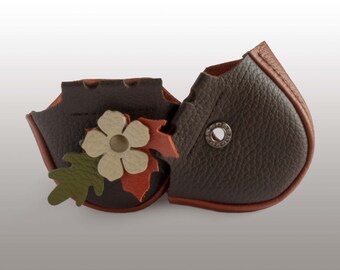 May include: A brown leather pouch with a decorative flower and leaf design. The pouch has a brown leather flap with a metal snap closure.