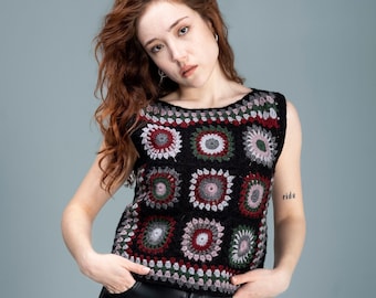 May include: A woman with long, curly red hair is wearing a black crochet top with colorful geometric patterns. She is also wearing black leather pants and has a tattoo on her arm that says "ride".