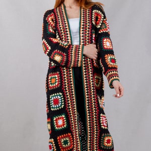 K&ouml;nnte beinhalten: Ein langer schwarzer H&auml;kelcardigan mit bunten geometrischen Mustern. Der Cardigan hat einen tiefen V-Ausschnitt und lange &Auml;rmel.