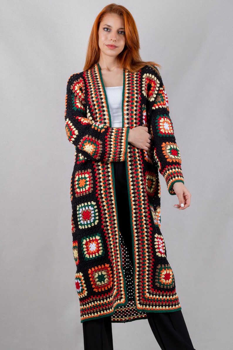 K&ouml;nnte beinhalten: Ein langer schwarzer H&auml;kelcardigan mit bunten geometrischen Mustern. Der Cardigan hat einen tiefen V-Ausschnitt und lange &Auml;rmel.