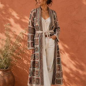 Può includere: Un lungo cardigan all'uncinetto aperto sul davanti con un motivo a piastrelle granny multicolore nei toni del marrone, verde acqua e crema. Il capo presenta maniche lunghe, una cintura da annodare, un top e pantaloni color crema.