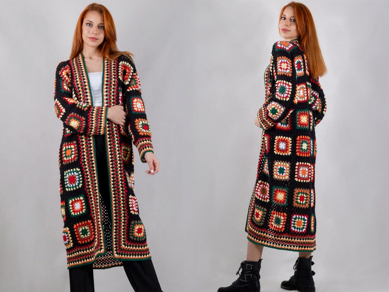K&ouml;nnte beinhalten: Ein langer schwarzer Cardigan mit einem bunten H&auml;kelmuster. Der Cardigan hat einen V-Ausschnitt und lange &Auml;rmel. Das Muster besteht aus Quadraten in verschiedenen Farben, darunter Rot, Orange, Gelb, Gr&uuml;n und Blau.