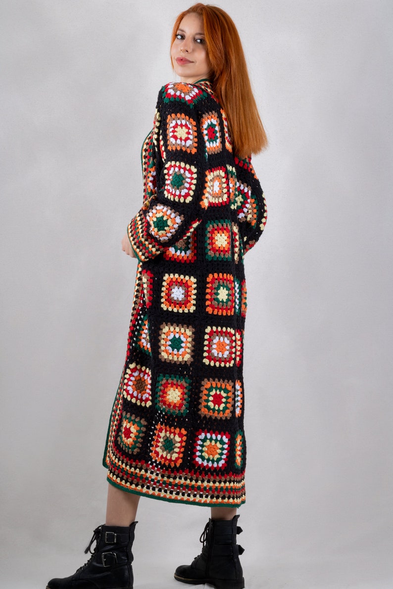 K&ouml;nnte beinhalten: Ein langer schwarzer H&auml;kelcardigan mit einem farbenfrohen geometrischen Muster. Der Cardigan hat eine lange, flie&szlig;ende Silhouette und ist aus verschiedenen Farben gefertigt, darunter Rot, Orange, Gelb, Gr&uuml;n und Wei&szlig;.