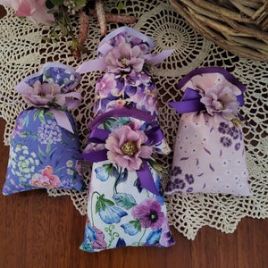 May include: Four small fabric pouches with floral patterns and purple ribbon ties. The pouches are filled with lavender and are perfect for adding a touch of fragrance to any room.