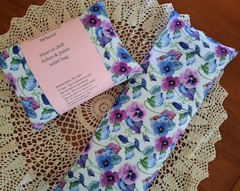 May include: Two wheat heat or chill aches and pains relief bags with a floral pattern of purple and blue pansies on a white background. The smaller bag has a pink label with the text "Wheat Heat or chill Aches & pains relief bag" and instructions for use.