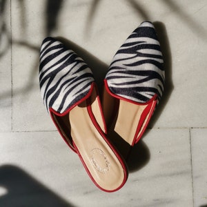 May include: A pair of black and white zebra print slip-on shoes with red trim.