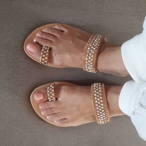 May include: A pair of brown leather sandals with gold straps adorned with rhinestones. The sandals have a toe ring design and are worn on a person's feet.