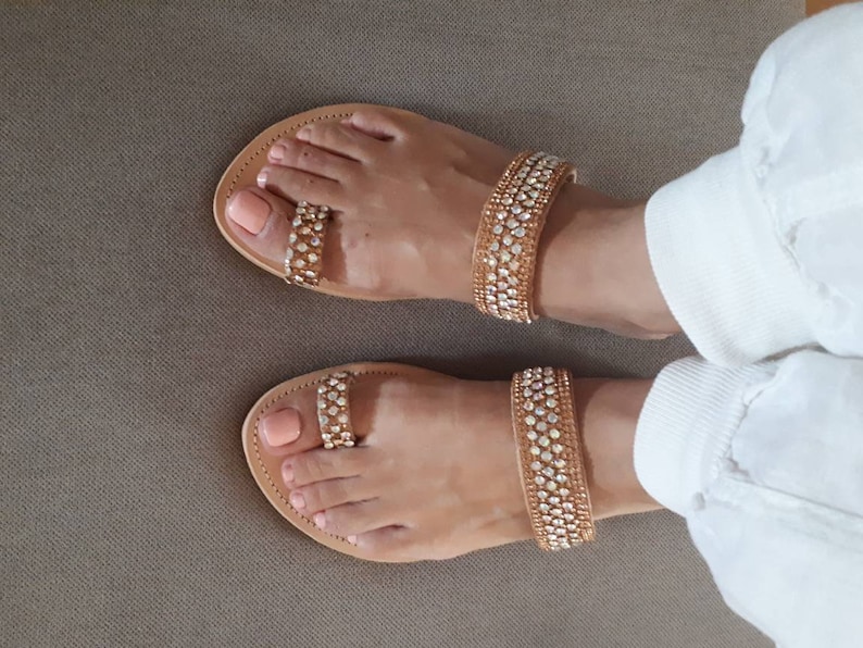 May include: A pair of brown leather sandals with gold straps adorned with rhinestones. The sandals have a toe ring design and are worn on a person's feet.