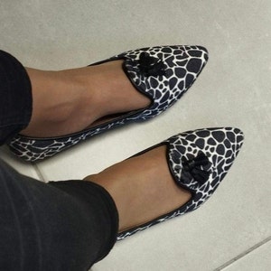 Könnte beinhalten: Ein Paar schwarz-weiß gemusterte Ballerinas mit spitzer Zehenpartie und einer kleinen schwarzen Schleife. Die Schuhe haben einen giraffeähnlichen Druck und sind für den Alltag geeignet.