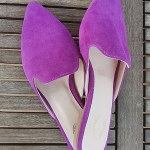 Puede incluir: Un par de zapatos de piel de ante morado con punta. Los zapatos tienen una plantilla marr&oacute;n claro y una etiqueta blanca en la parte inferior.