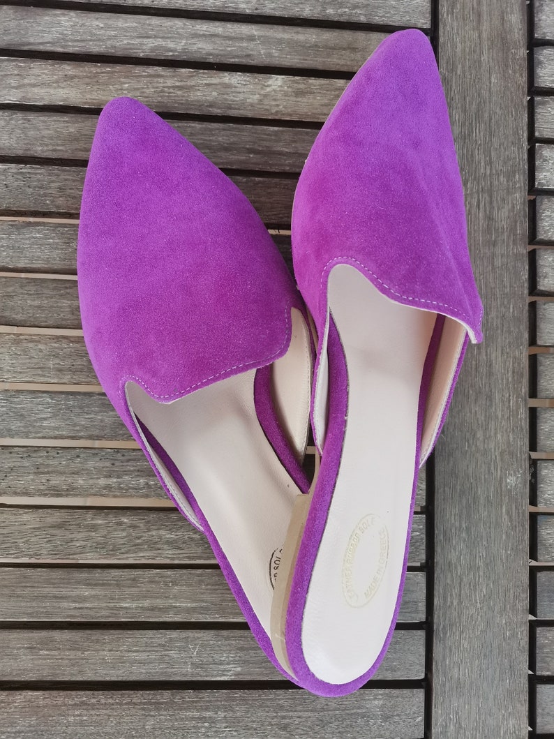 Puede incluir: Un par de zapatos de piel de ante morado con punta. Los zapatos tienen una plantilla marr&oacute;n claro y una etiqueta blanca en la parte inferior.