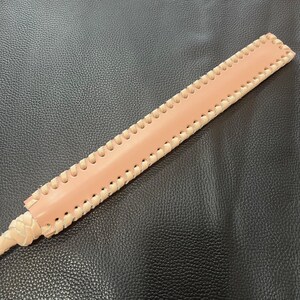 May include: A long, light brown leather whip with a braided handle and decorative stitching along the edges.