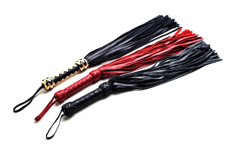 May include: Three leather whips in black, red, and black. The handles are braided, with a loop at the end. One handle is black and tan, the other two are red and black. The whips have long, thin leather strands.