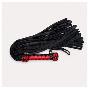 May include: A black leather flogger with a red and black braided handle. The flogger features multiple long, thin leather strands. The handle is cylindrical with a braided design in red and black.