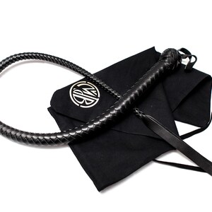 Op de afbeelding: Een zwarte leren zweep met een gevlochten handvat en een zwarte stoffen tas met een gouden monogram.