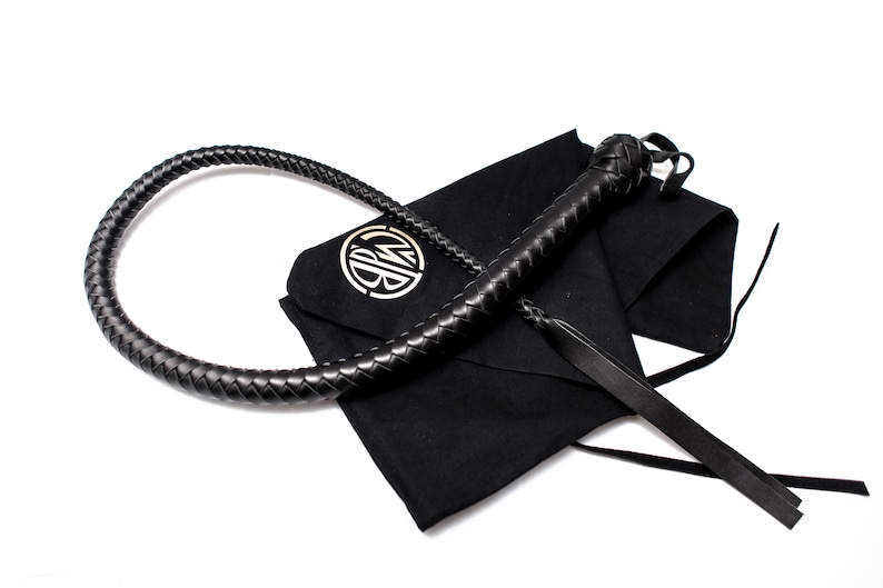 Op de afbeelding: Een zwarte leren zweep met een gevlochten handvat en een zwarte stoffen tas met een gouden monogram.