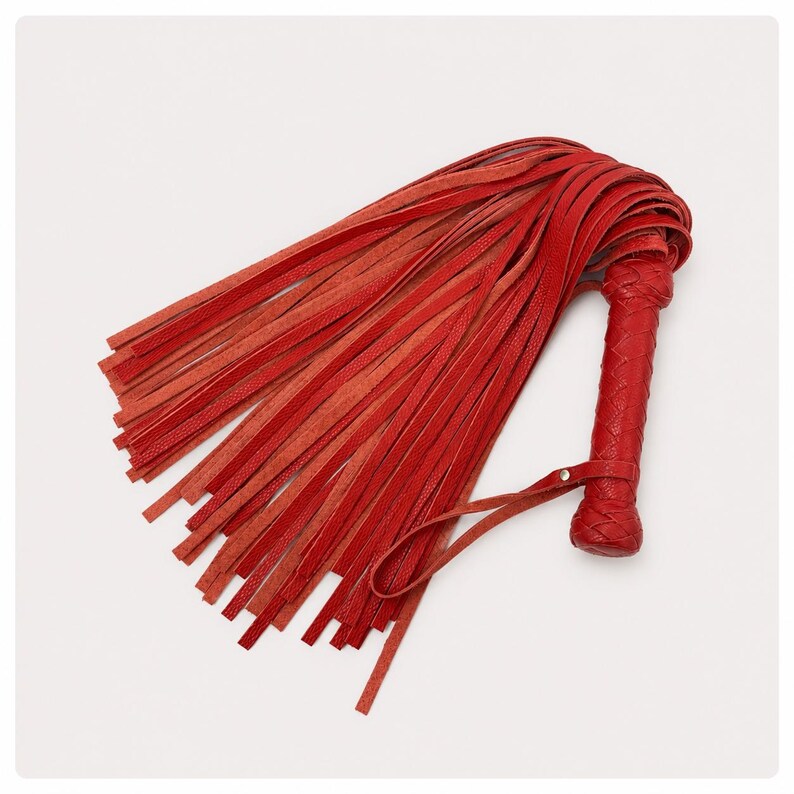 May include: A red leather flogger with a braided handle and numerous long, thin leather strands. The handle features a wrist strap. The flogger is a deep red color and is set against a white background.