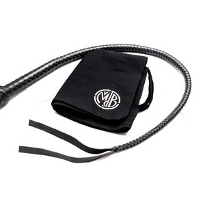Op de afbeelding: Een zwarte leren zweep met een gevlochten handvat en een zwarte stoffen tas met een wit monogram.