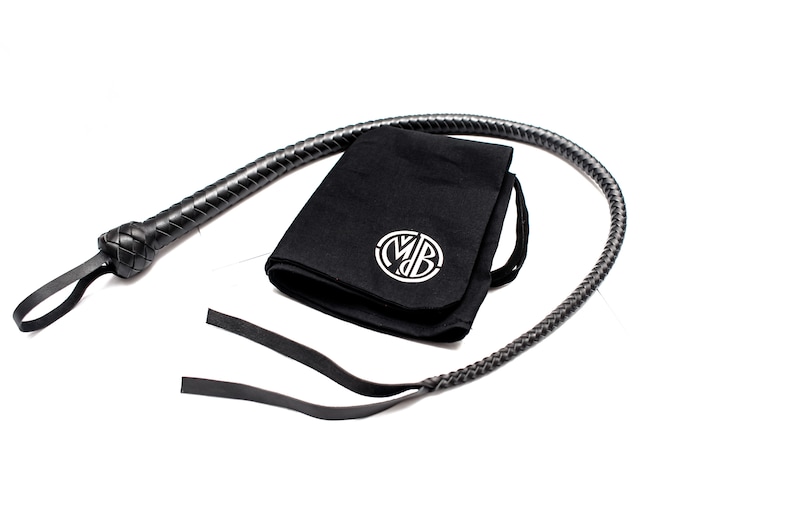 Op de afbeelding: Een zwarte leren zweep met een gevlochten handvat en een zwarte stoffen tas met een wit monogram.
