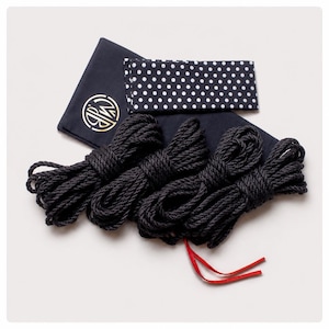 May include: Four coils of black rope arranged in a row, accompanied by a dark navy blue fabric pouch featuring a gold circular logo and a separate rectangular fabric piece with a white polka dot pattern on a dark navy blue background.