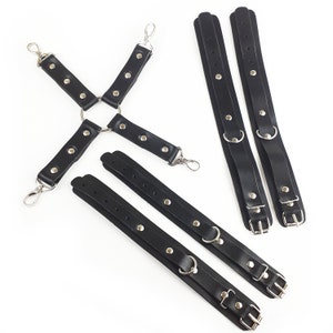 May include: A set of black straps featuring silver-toned metal hardware, including four adjustable cuffs with buckles and D-rings, and a central cross-shaped connector piece with four swivel lobster claw clasps at the ends of each strap.