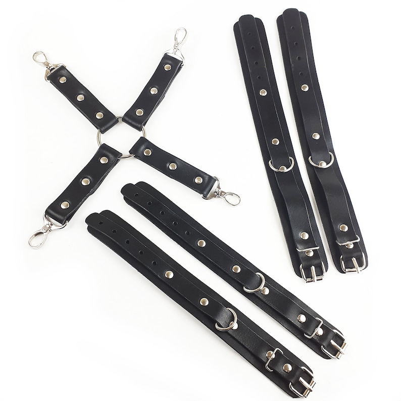 May include: A set of black straps featuring silver-toned metal hardware, including four adjustable cuffs with buckles and D-rings, and a central cross-shaped connector piece with four swivel lobster claw clasps at the ends of each strap.