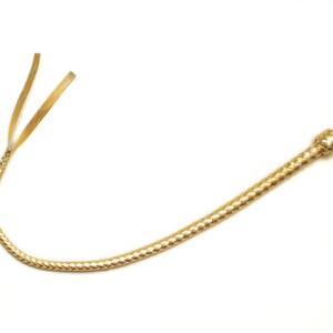 Op de afbeelding: Een gouden leren zweep met een gevlochten ontwerp en een geknoopte handgreep.