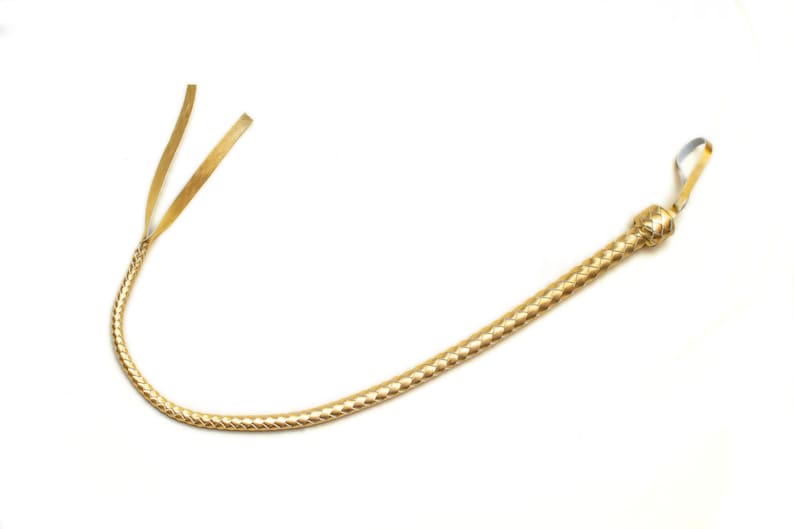 Op de afbeelding: Een gouden leren zweep met een gevlochten ontwerp en een geknoopte handgreep.