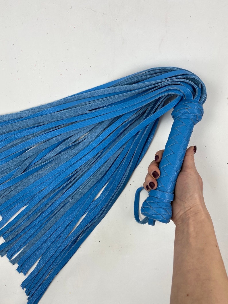 May include: A blue leather flogger with a braided handle and numerous long, thin leather falls. The handle has a loop for grip. The flogger is a solid blue color.