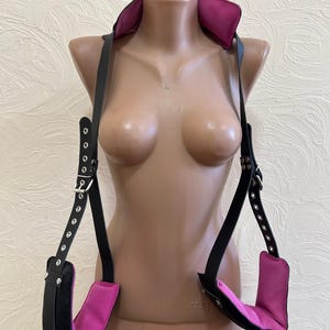 May include: Black leather harness with pink padded straps and silver buckles. The harness has adjustable straps and is designed for hanging.