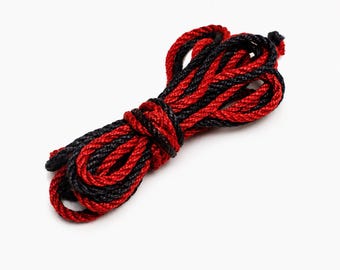 May include: A coiled length of braided cord featuring a two-tone design with alternating strands of black and vibrant red fibers. The rope is tightly wound into a compact bundle, showcasing a consistent twisted texture throughout the entire length.