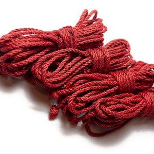 Könnte beinhalten: Ein Haufen rotes Seil, zusammengerollt und verknotet. Das Seil ist dick und strukturiert und scheint aus Naturfasern zu bestehen.