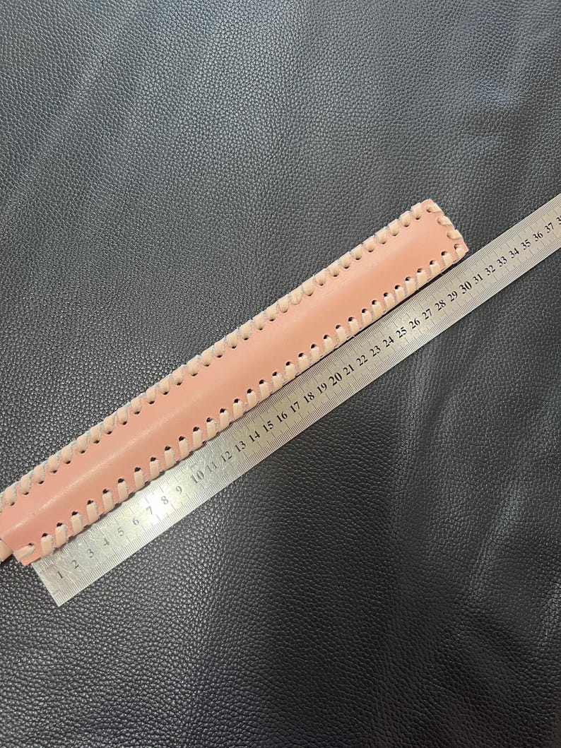 May include: A pink leather strap with a decorative stitch pattern. The strap is measured with a ruler, showing a length of 37 inches.