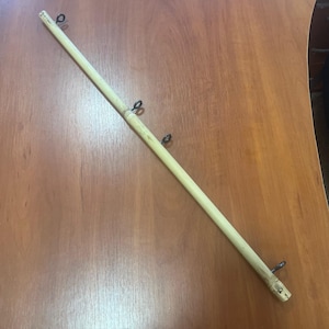 May include: A long, light brown wooden rod with four metal rings attached. The rod is lying on a wooden surface.