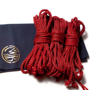 May include: Three spools of red rope, each tied in a knot, are arranged on a dark blue fabric bag with a gold logo.