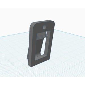 May include: A gray, rectangular 3D-printed object with a hole at the top and a rectangular opening in the center. The object has a small base and a slightly angled design.