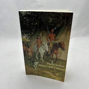 Op de afbeelding: Een hardcover boek getiteld "Plains Indian History and Culture" met een omslagillustratie van indianen te paard en een hond. De omslag van het boek is sepia met tekst in wit en zwart.