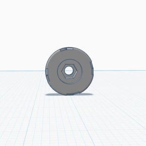 Puede incluir: Un objeto circular gris con un agujero hexagonal en el centro. El objeto tiene una serie de muescas rectangulares alrededor del borde exterior. El diseño es simple y geométrico.