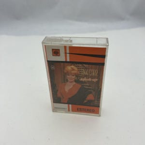 May include: A vintage cassette tape featuring Bikki Carr. The cassette case is clear plastic with an orange and white design. The album cover shows a woman in an orange top and black shawl. The word "STEREO" is printed in red.