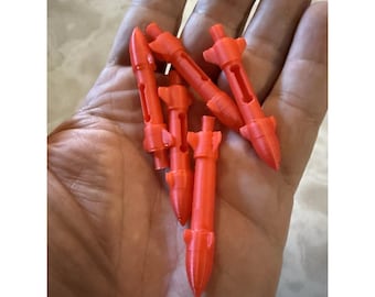 May include: A collection of small, orange, 3D-printed rocket-shaped toys. Each toy has a pointed nose, fins, and a central slot. The toys are held in a person's hand.