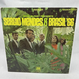 May include: Vintage vinyl record album cover for "Sergio Mendes & Brasil '66." The cover features a group of people in suits and dresses, set against a backdrop of lush green foliage. The album title is in large yellow letters.