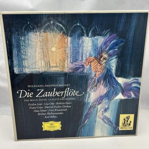 May include: A vintage record album cover featuring a watercolor illustration of a person in a blue and purple feathered costume playing a flute. The album is titled "Die Zauberflöte" by Wolfgang Amadeus Mozart. The album cover also includes the text "The Magic Flute La Flute Enchantée" and lists the performers and orchestra.