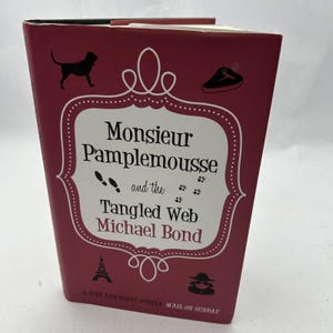 Può includere: Una copertina di libro rossa con un bordo bianco e illustrazioni nere. Il titolo è "Monsieur Pamplemousse e la ragnatela intricata" di Michael Bond. La copertina del libro include anche il testo "Un puzzle fine e divertente Mail on Sunday".