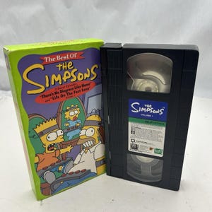 Può includere: Un cofanetto VHS e un set di scatole dei Simpson, con gli episodi "Non c'è vergogna come a casa" e "La vita sulla corsia veloce". La copertina della scatola presenta Homer, Bart e Lisa Simpson in un videogioco.
