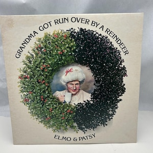 May include: A vintage record album cover featuring a woman wearing a white hat and glasses, holding a cup of coffee. The woman is framed by a green and black wreath with the text "Grandma Got Run Over By A Reindeer" and "Elmo & Patsy" on the cover.