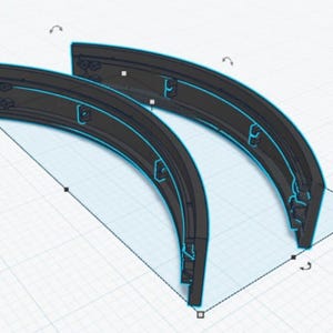 May include: Two curved, dark grey architectural components with a light blue outline. The pieces have small, rectangular cutouts along the edges. The design is set against a white background with a grid pattern.